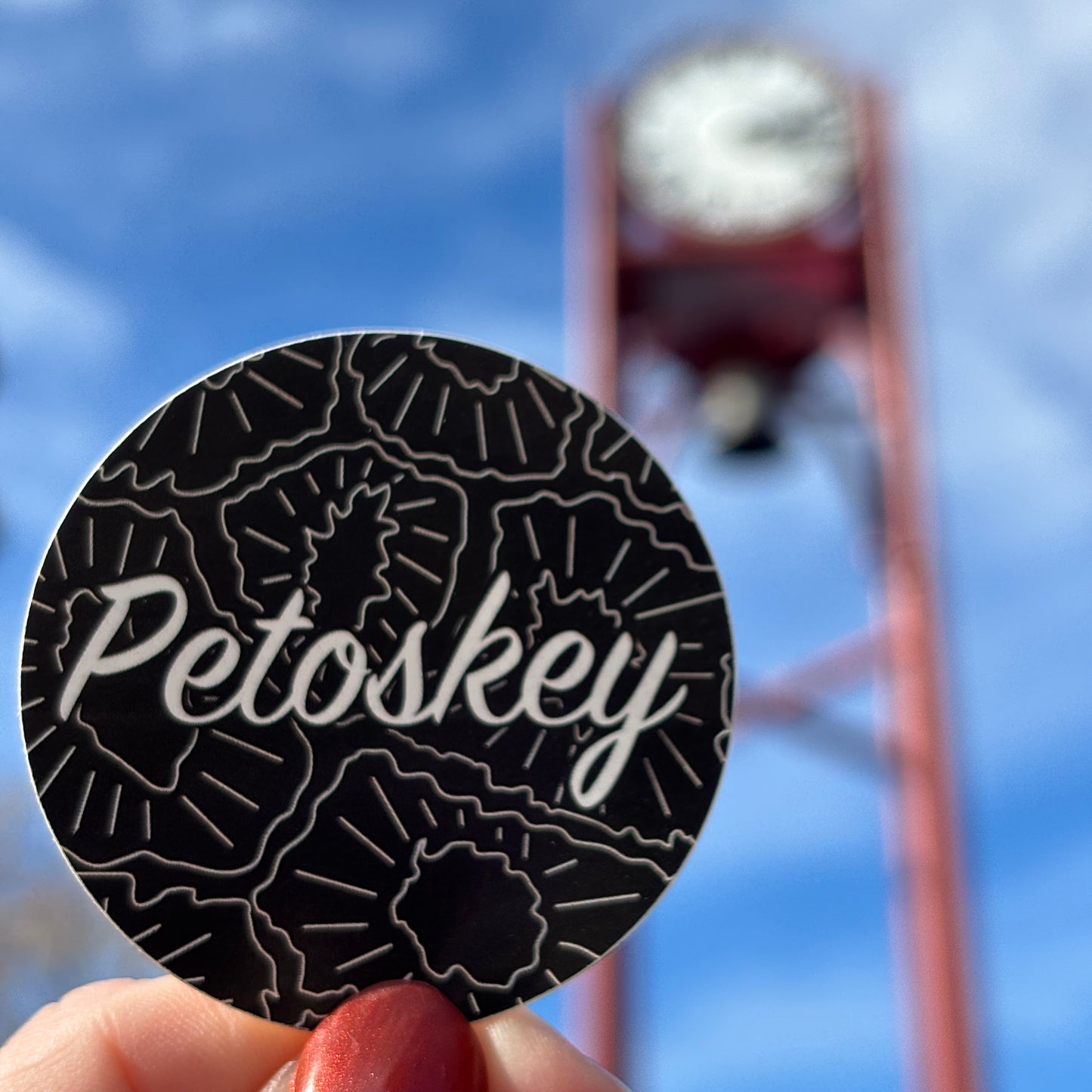 Round black sticker with 'Petoskey' text held against a blurred background