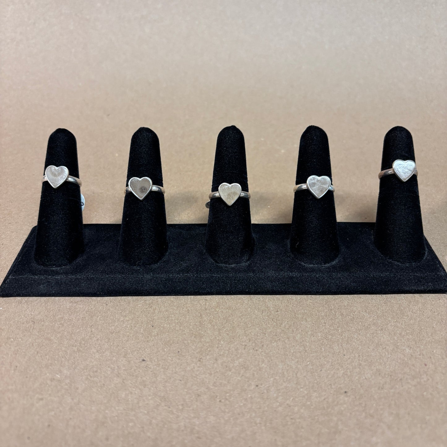 Set of five silver heart-shaped Petoskey Stone rings on black ring stands against a beige background