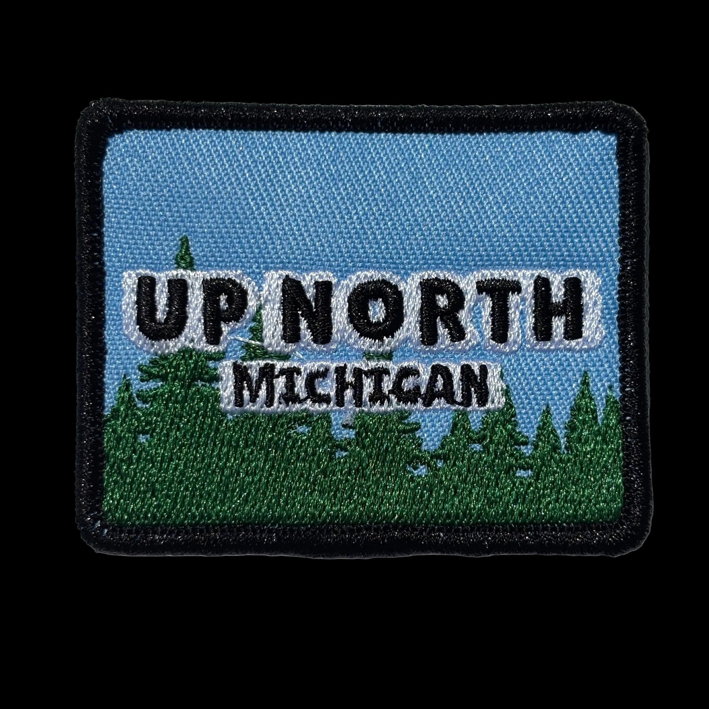 Embroidered patch with 'Up North Michigan' text on a blue sky and green tree landscape background.