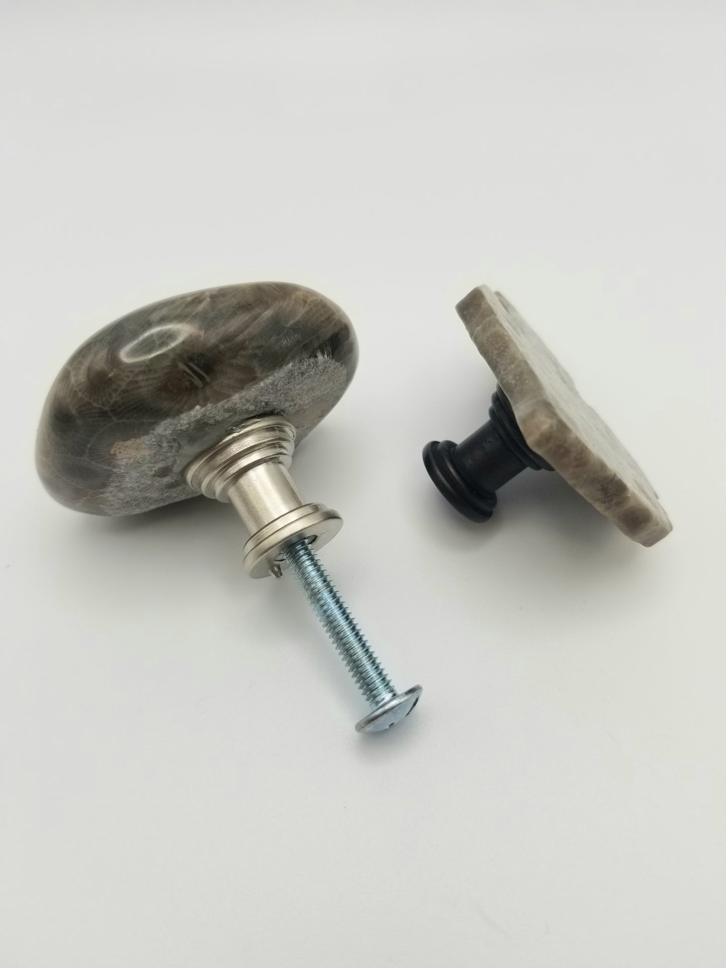 An image of two of the petoskey stone cabinet knobs. One is facing away and shows the silver backing with a screw in it. The other is a side view of the michigan mitt knob with a bronzed backing.