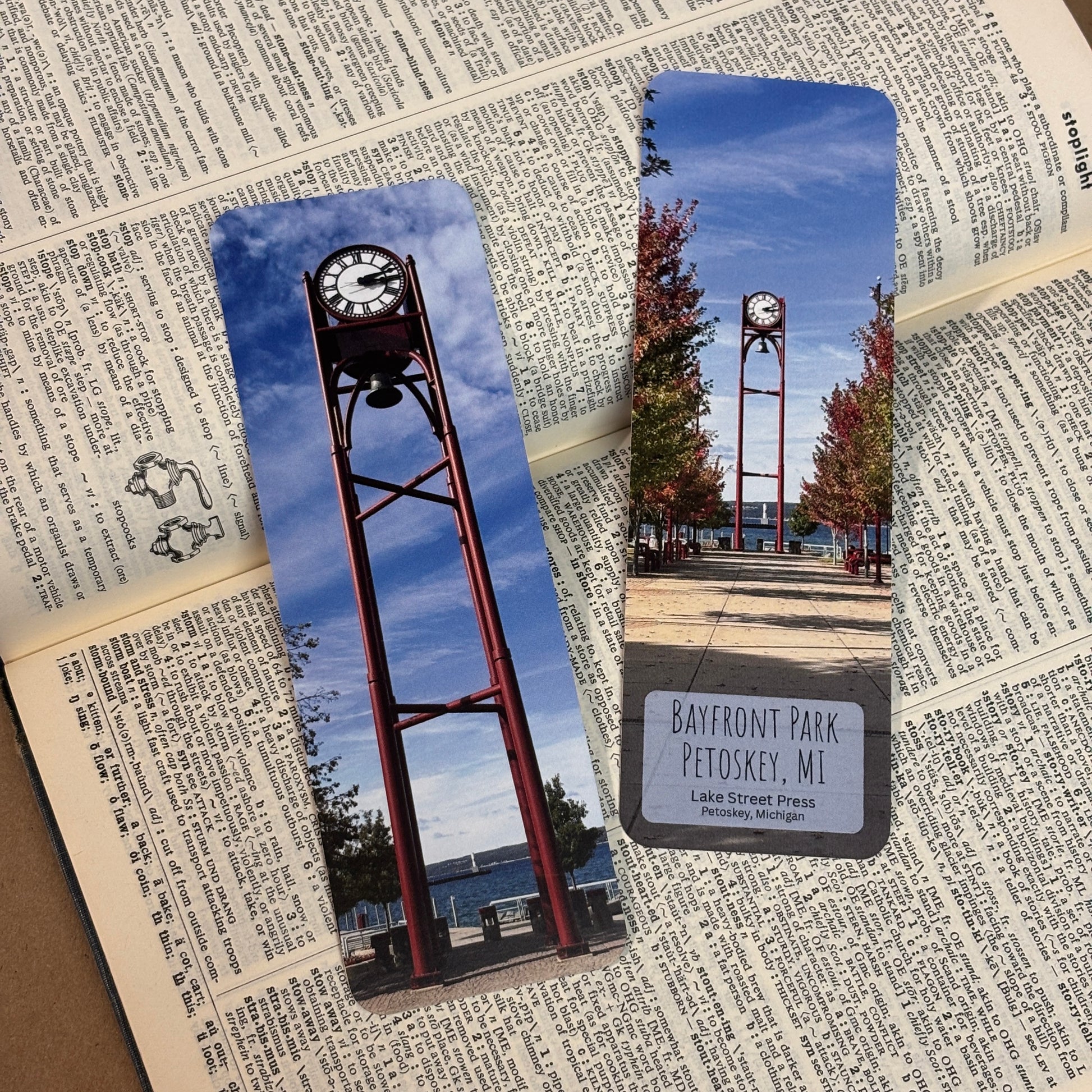 Two rectangular bookmarks printed with a scenic photograph of Petoskey's Bayfront park clock tower displayed on top of an open book with printed text.