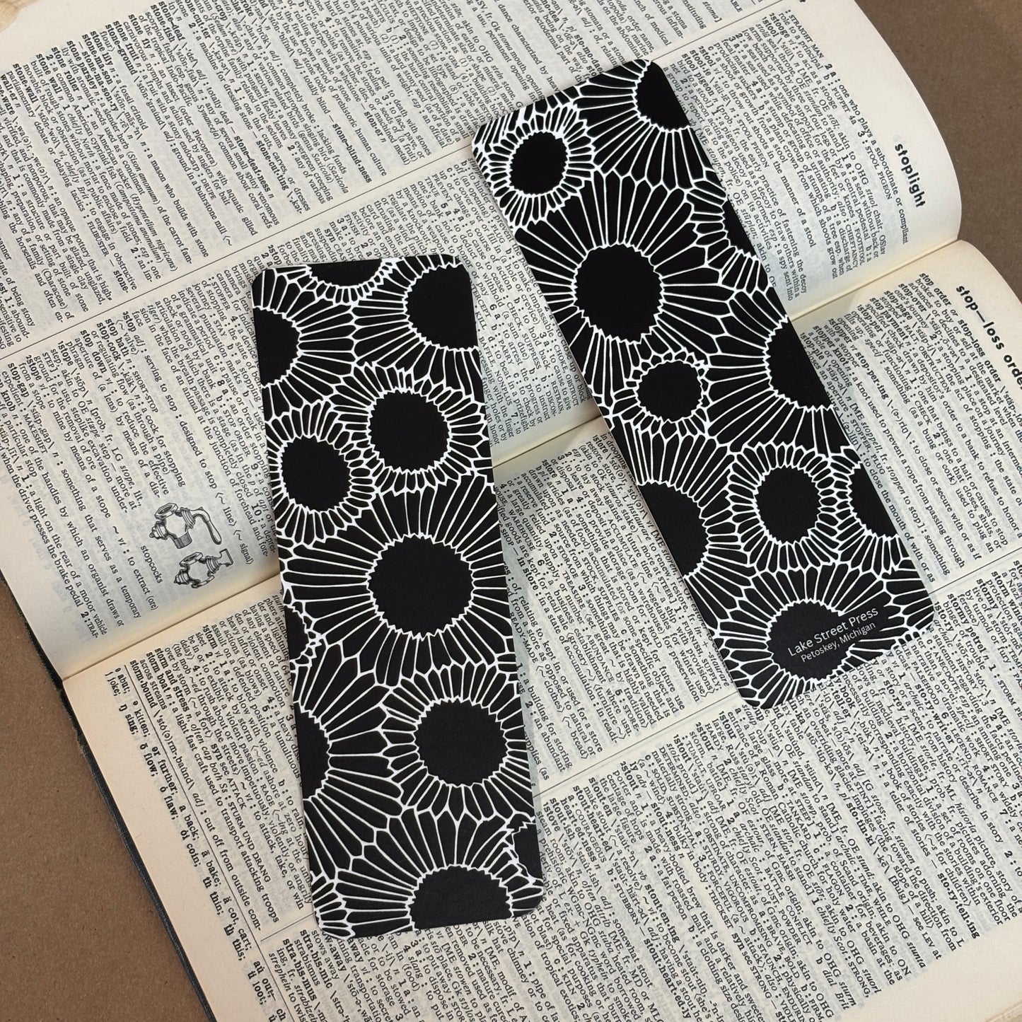Two black and white patterned bookmarks with a petoskey stone line drawing design, resting on an open book with printed dictionary pages.