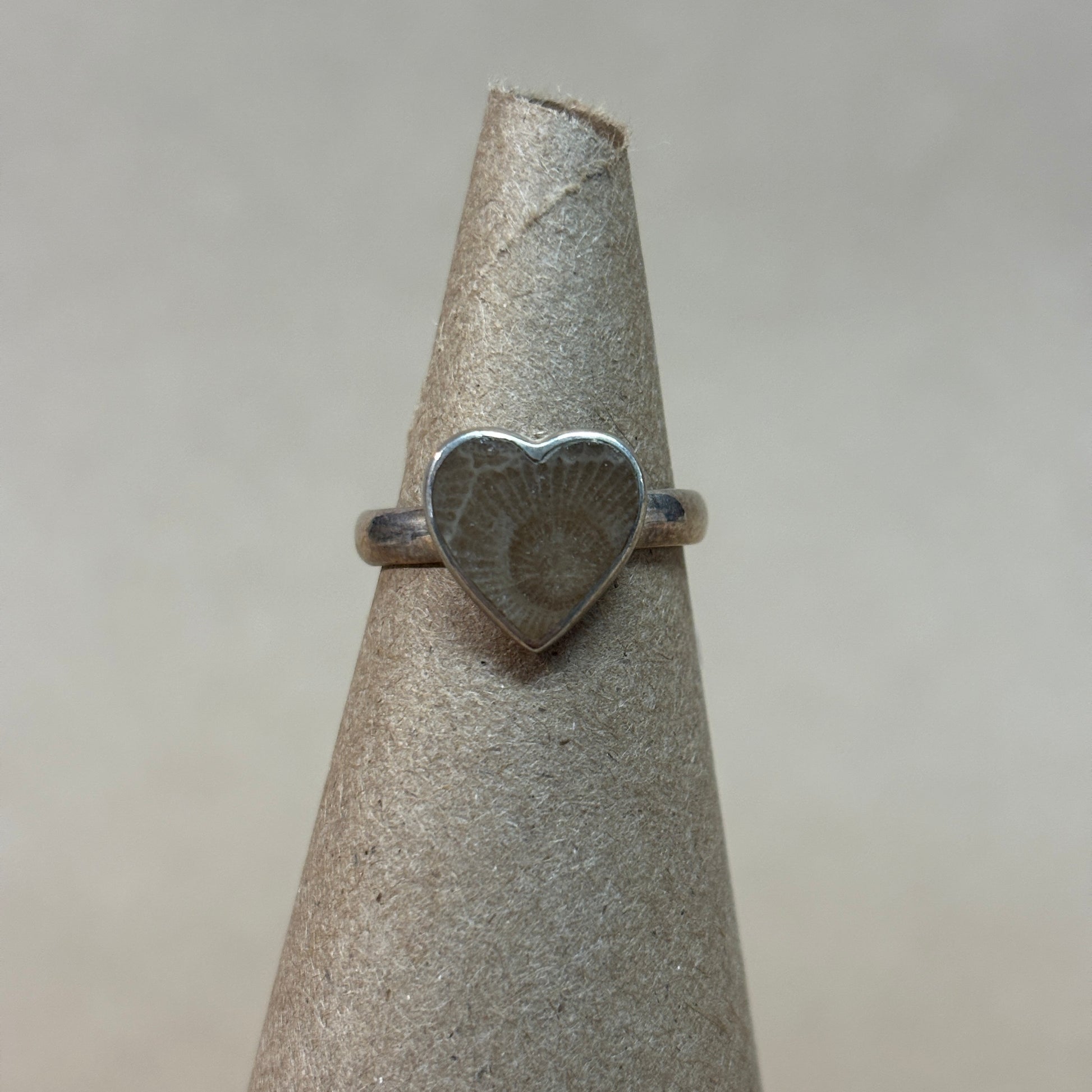 Silver heart-shaped petoskey stone ring on a gray stand with a neutral background