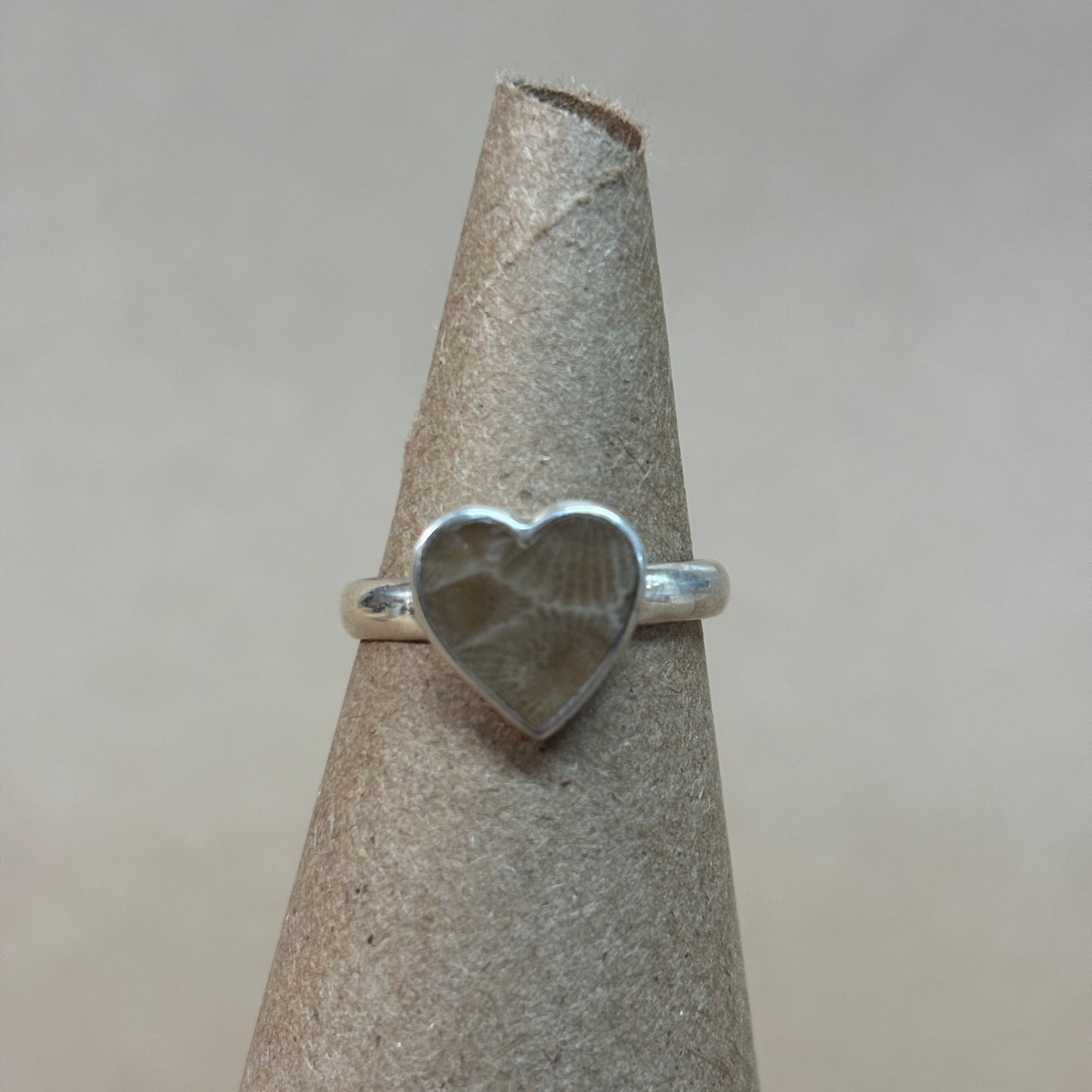 Silver heart-shaped petoskey stone ring on a gray stand with a neutral background