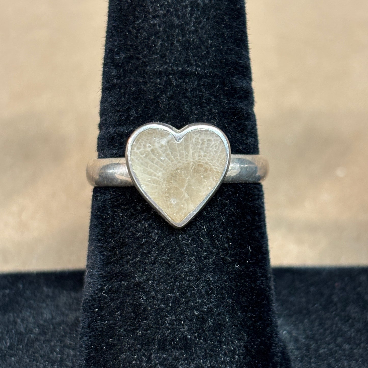 Sterling Silver heart-shaped Petoskey Stone ring on a black stand with a beige background