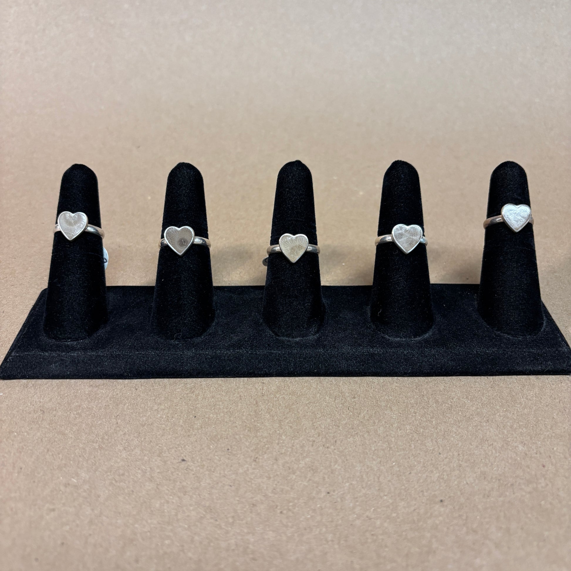 Set of five silver heart-shaped Petoskey Stone rings on black ring stands against a beige background