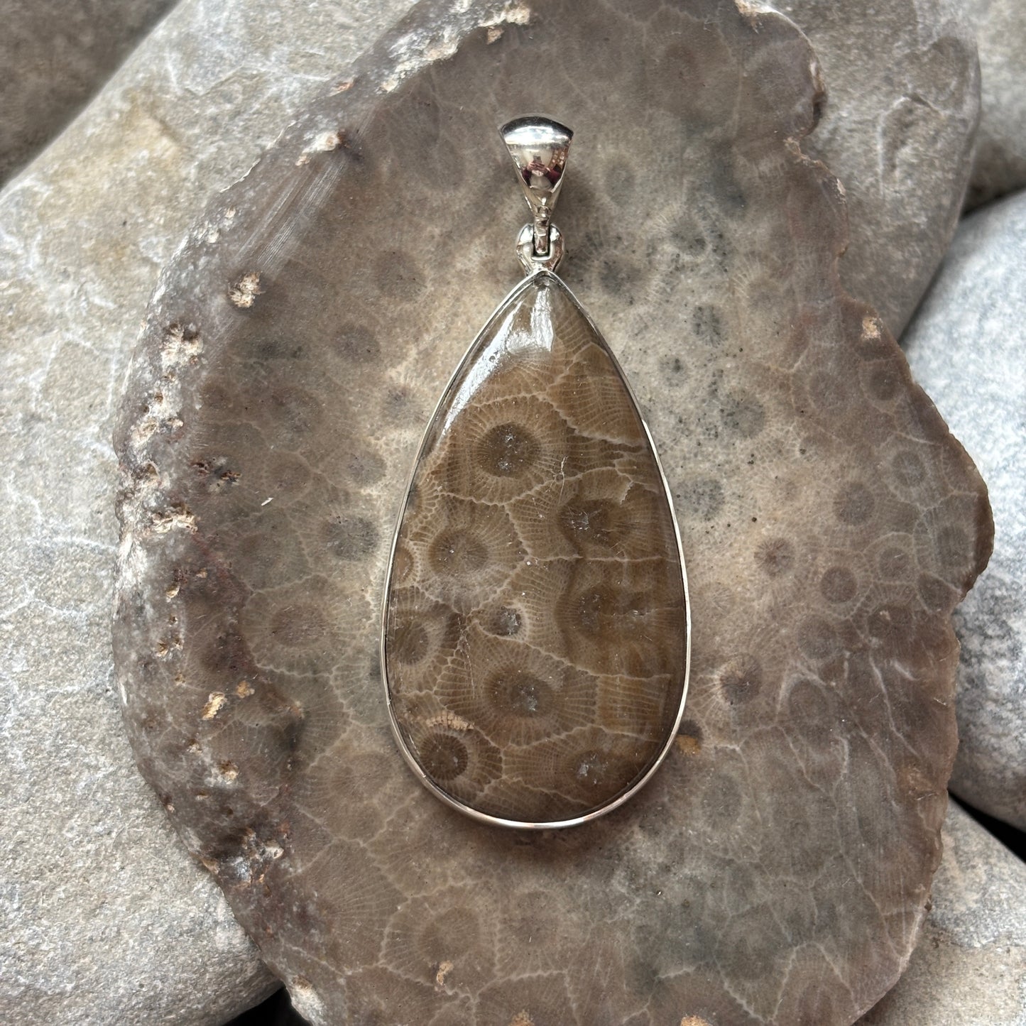 Teardrop-shaped pendant with a textured design on a Petoskey stone surface
