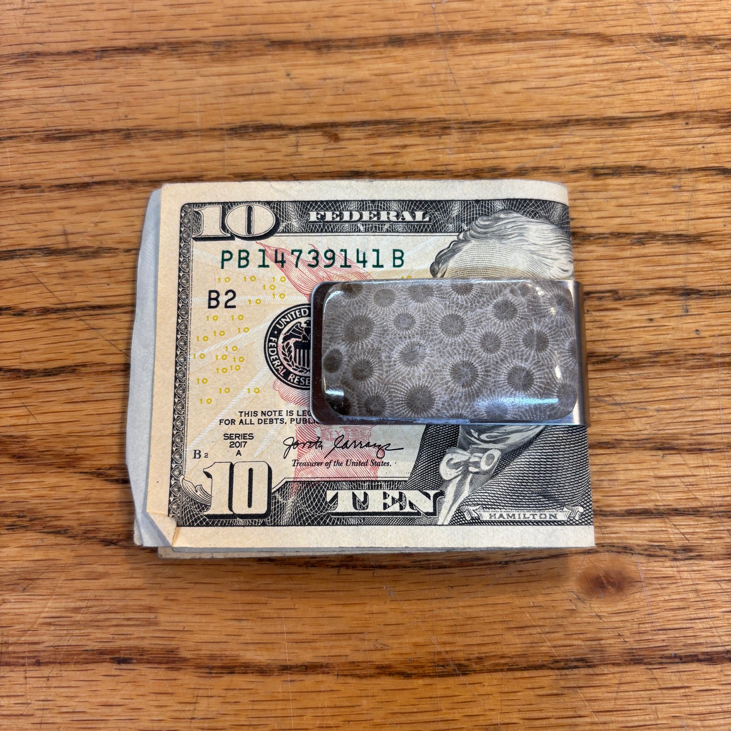 Ten-dollar bill folded over a metal money clip with petoskey stone on a wooden surface
