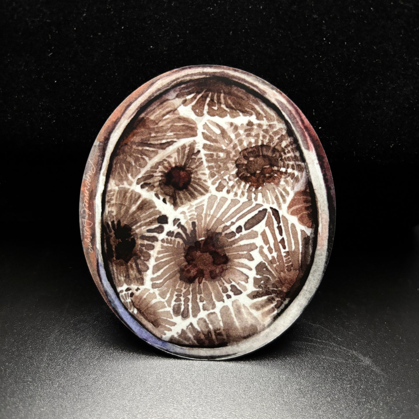 Round oval sticker with a watercolor petoskey stone pattern on a black background