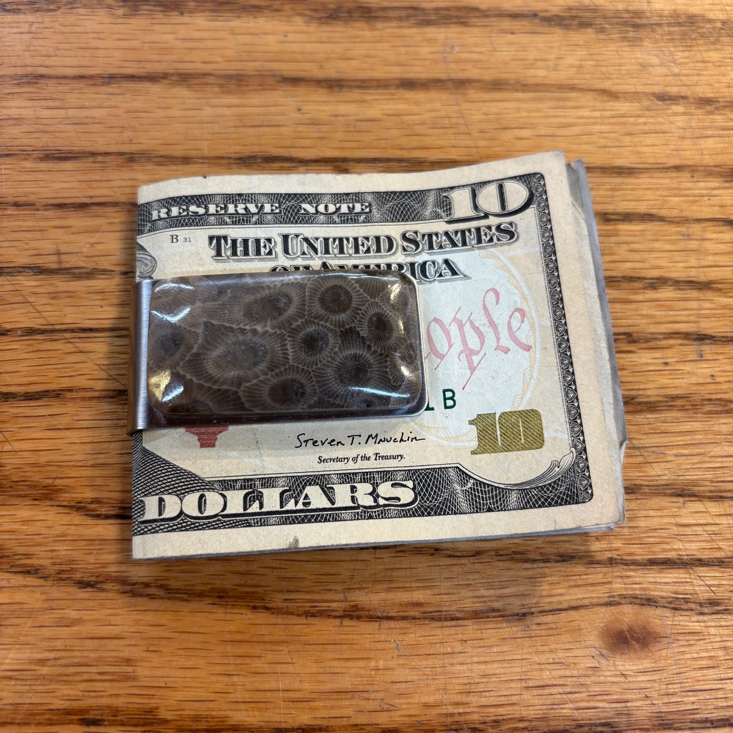 Ten-dollar bill with a metal money clip with a petoskey stone on a wooden surface