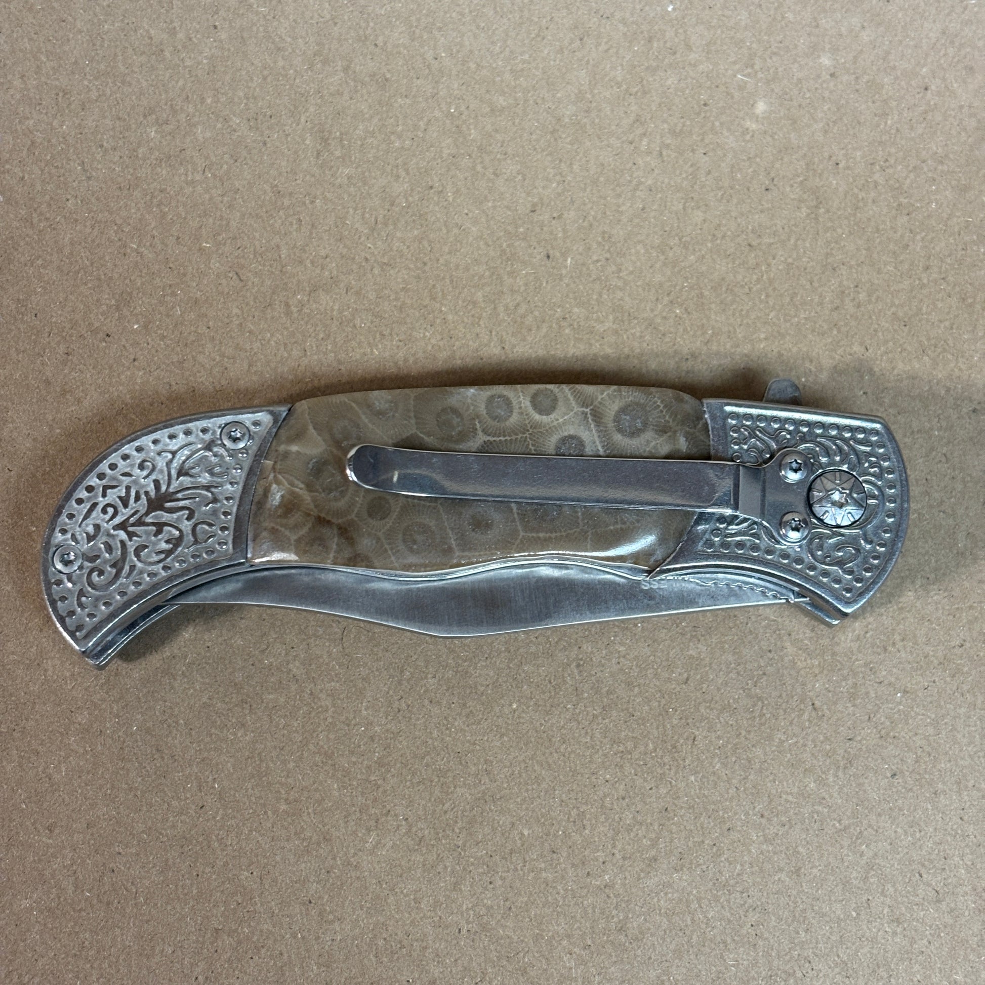 Folding knife with decorative Petoskey stone handle showing the back with a belt clip on a beige background