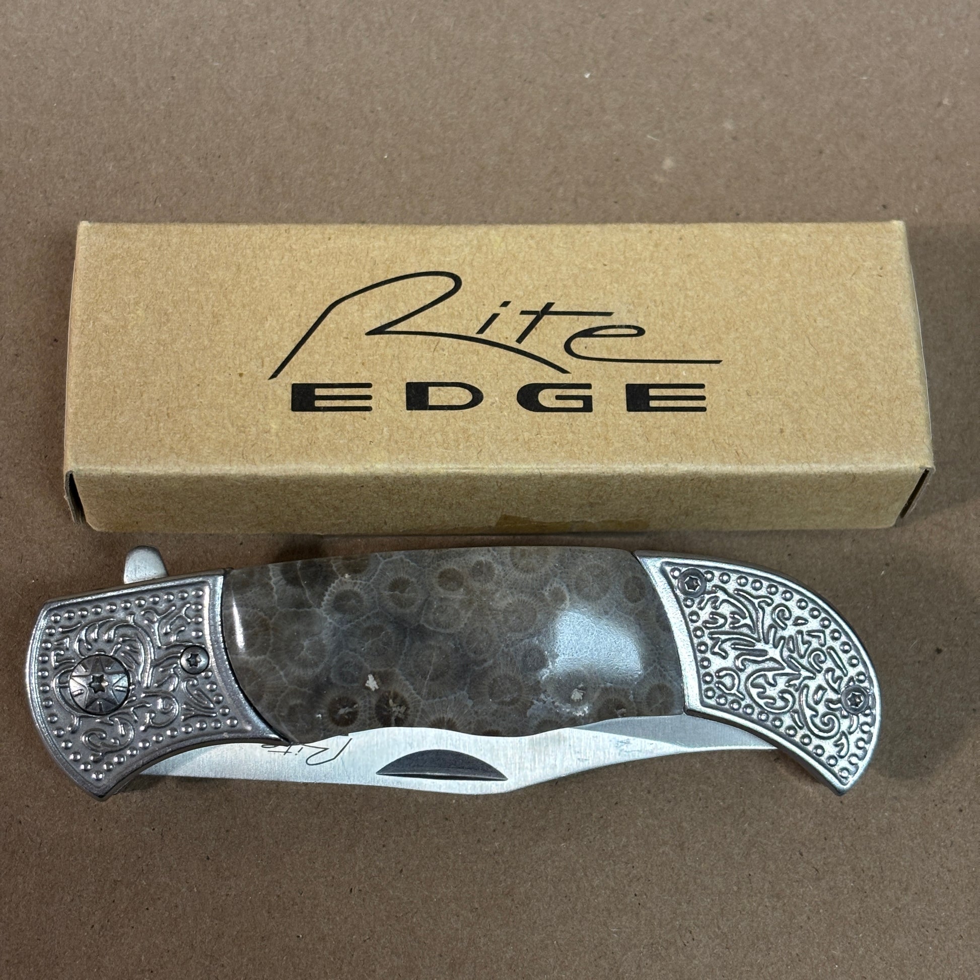 Folding knife with decorative handle on a brown surface, accompanied by a 'Rite Edge' branded box.