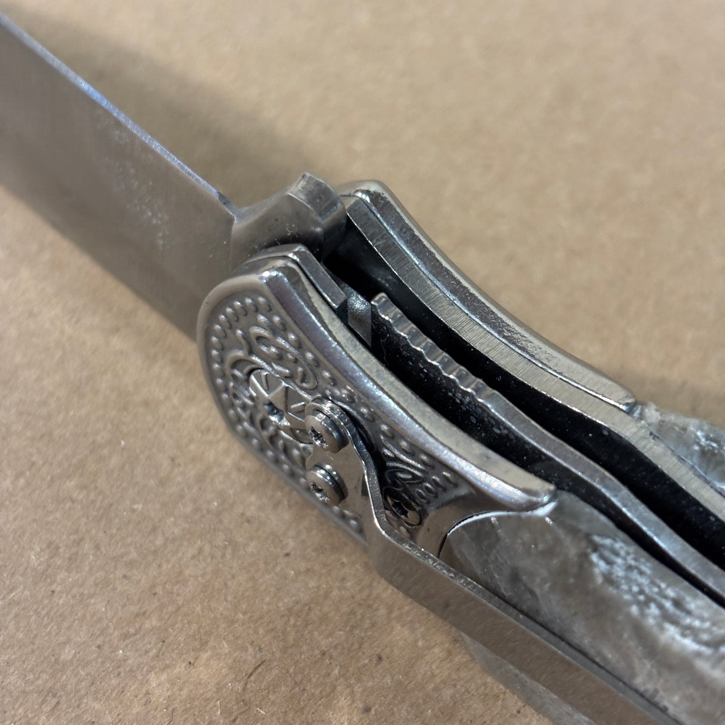 Close-up of a folding knife showing the safety lock and belt clip with decorative Petoskey stone handle on a beige background