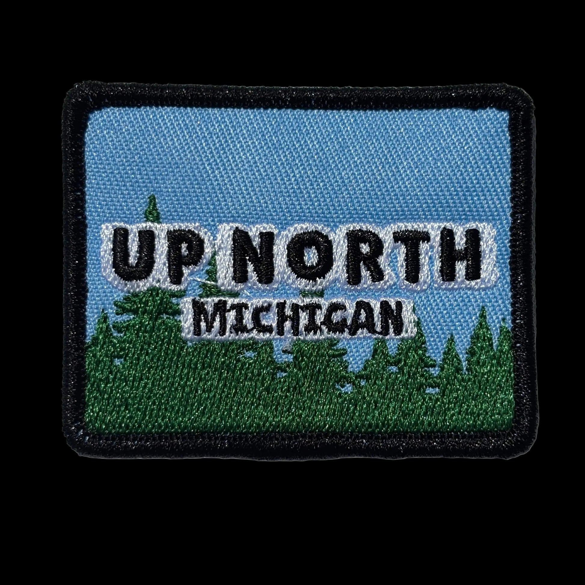 Embroidered patch with 'Up North Michigan' text on a blue sky and green tree landscape background.