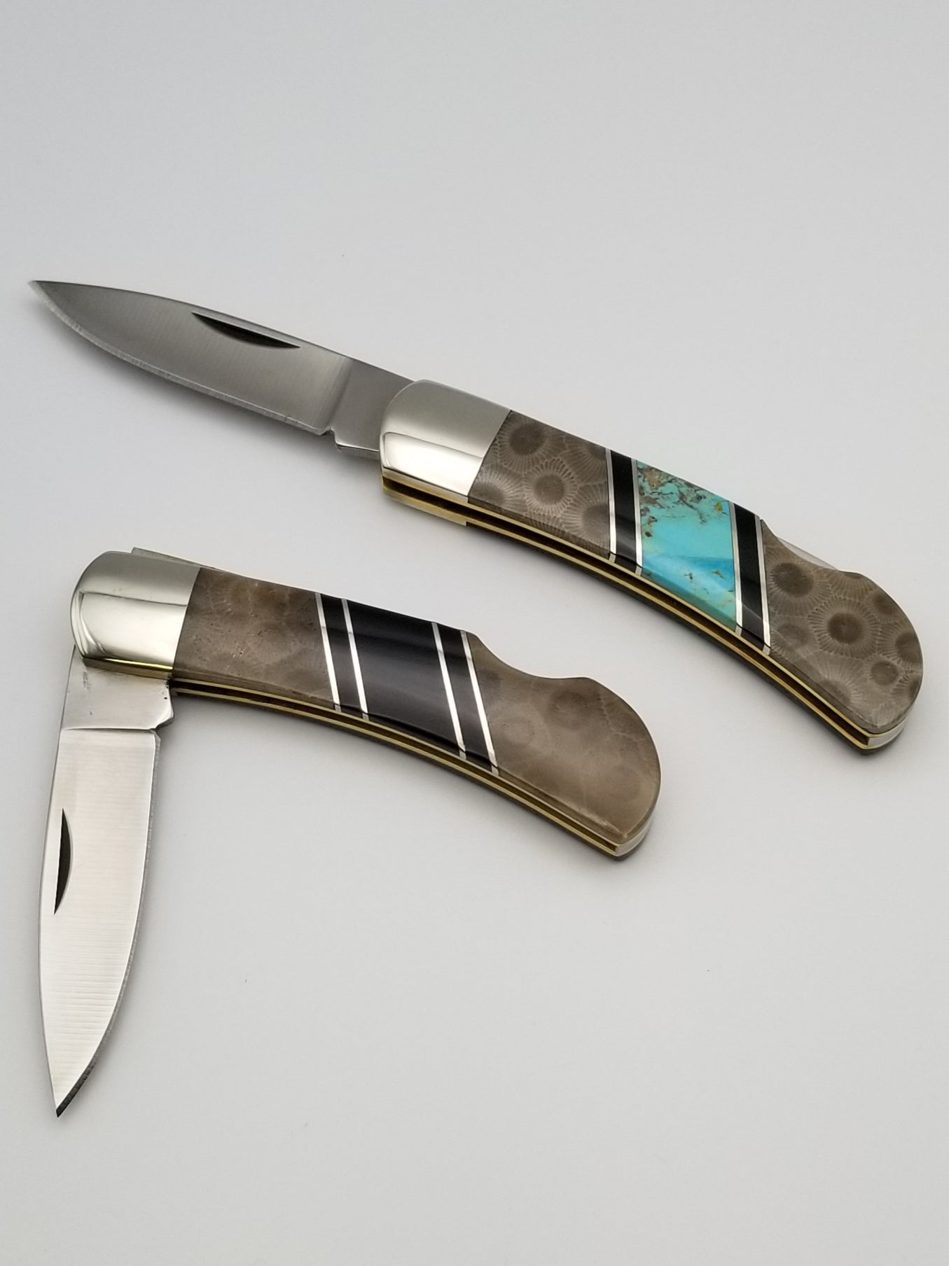 Top knife is fully opened and has a turquoise inlay between two Petoskey stone inlays. Bottom pocket knife is half opened and has a black amber inlay between the petoskey stone inlays.