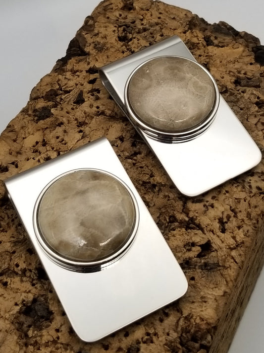 Silver money clips side by side facing upward on a block of cork. Both feature a good sized petoskey stone in a circle embellishment center top.