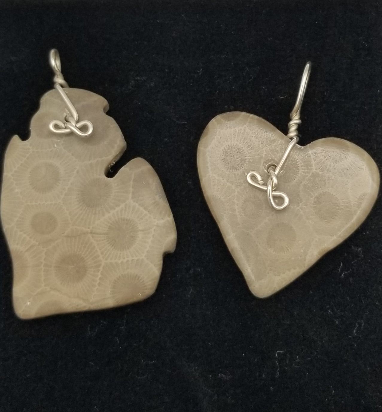 Two large petoskey stone charm pendants with sterling silver wire wrapped bails. The bails feature a twisted bow/infinity shape at the bottom. The left charm is shaped into the lower peninsula of Michigan and the right one is shaped into a classic heart shape.