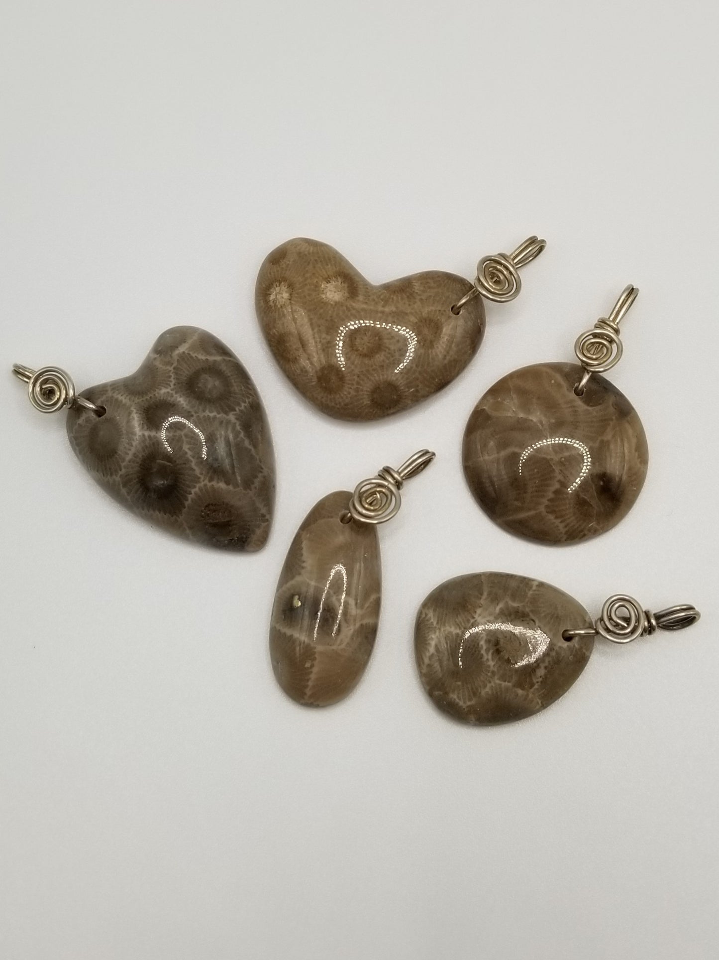 Five impeccably polished petoskey stone charms that have been wire wrapped for the bail and include a small wire spiral where the bail meets the stone. Two of the petoskey stone charms are shaped into subtle hearts, one is a near-perfect circle, one is an oval, and the last is a subtle tear drop shape. Michigan made.