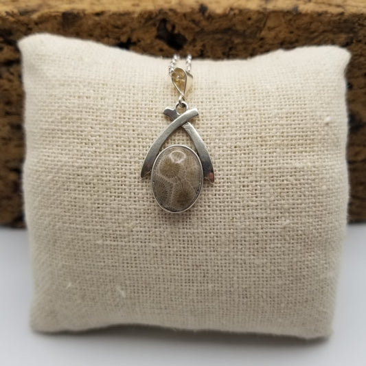 Vibrant oval petoskey stone set under a dainty set of .925 sterling silver arches on an 18 inch silver chain. The necklace lays over a small pillow covered in a canvas fabric. Stamped .925. Handmade in Michigan.