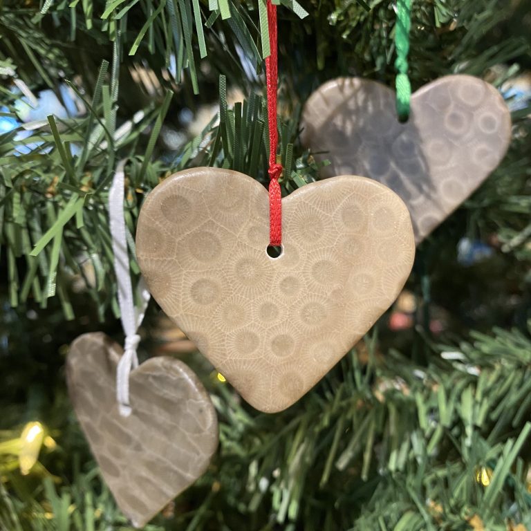 Image of three (3) petoskey stone ornaments shaped into hearts with a hole drilled and a ribbon tied on. They are all hanging on a christmas tree.