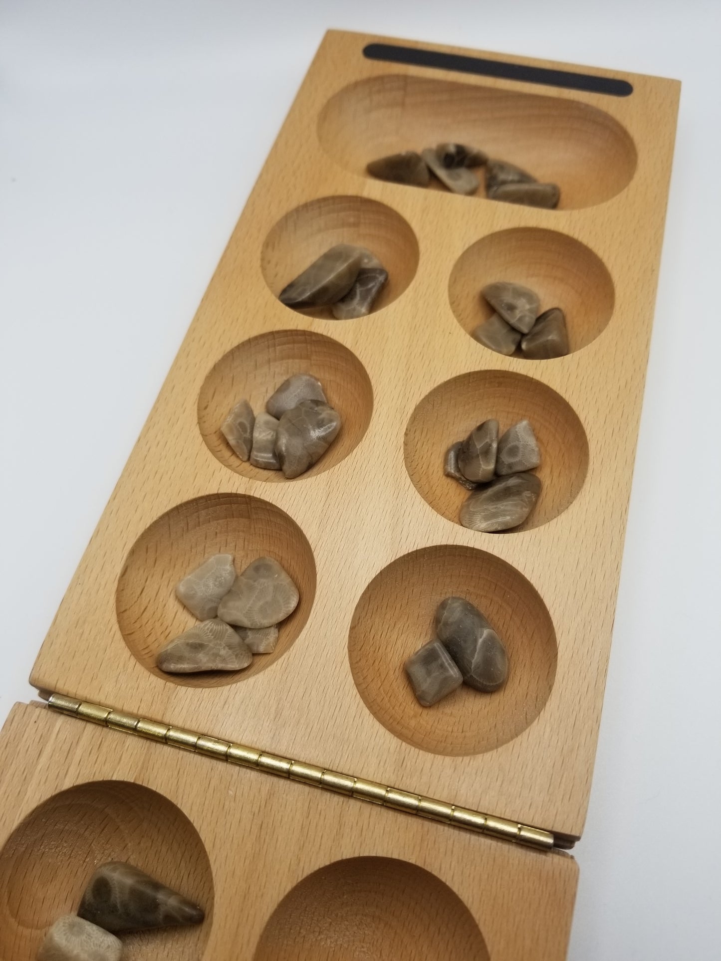 Close up of our tan mancala board with two to four petoskey stone pebbles in each indented space. 