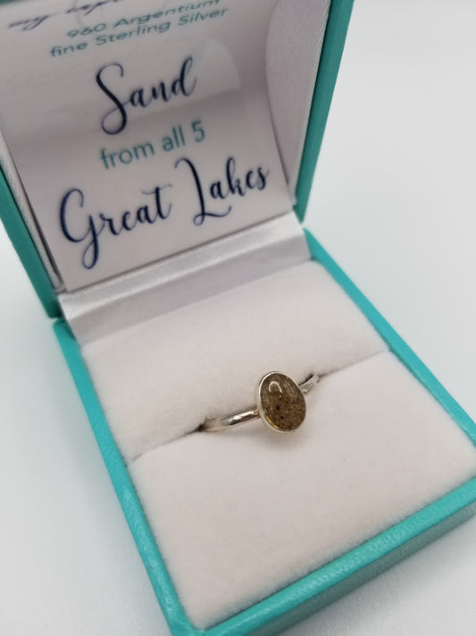 .960 Argentium sterling silver thin banded ring with sand from the five great lakes set in clear resin. Ring is set in a robin's egg blue box that is opened toward the camera and reads "sand from all 5 great lakes"
