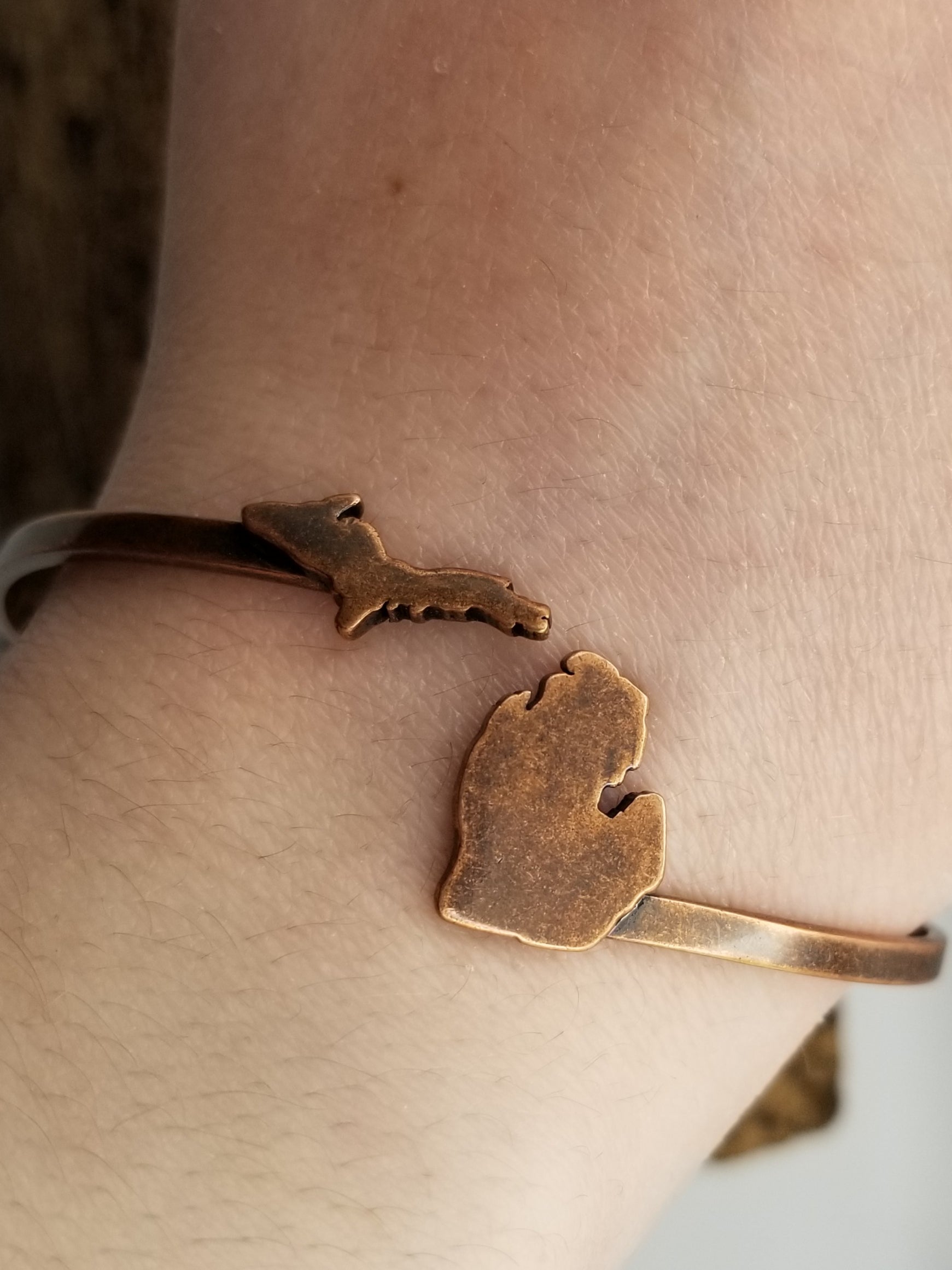 Close up image of the antiqued copper wrap around adjustable cuff. Features Michigan's upper peninsula on the left side and the lower peninsula on the right. The cuff is shown worn on a woman's wrist.