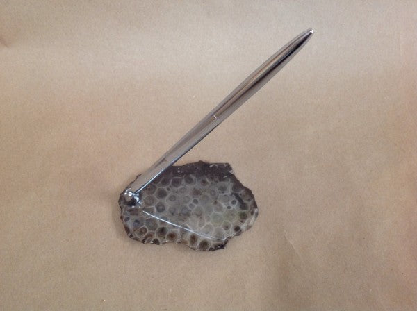 Silver pen attached to a small petoskey stone slab on a piece of kraft paper. Pen holder comes with the pen.