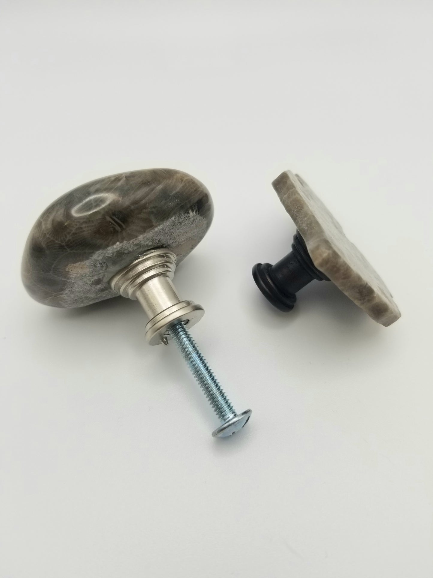 An image of two of the petoskey stone cabinet knobs. One is facing away and shows the silver backing with a screw in it. The other is a side view of the michigan mitt knob with a bronzed backing.