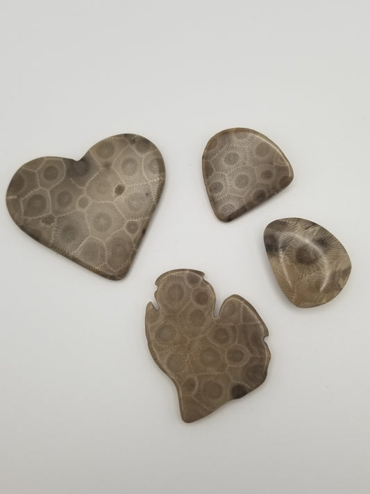 Four (4) petoskey stone magnets on a white background. Two (2) are natural stone shaped, one is a large heart, and the last is shaped into the lower peninsula of Michigan. All are neatly hand polished.
